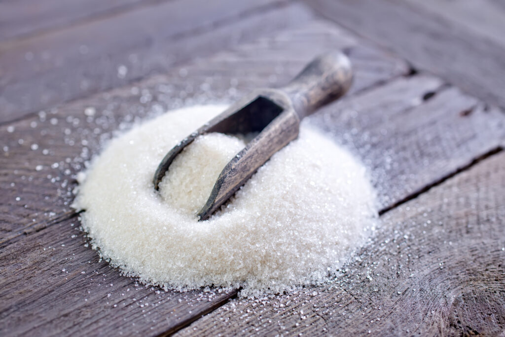 A heap of granulated sugar with a rustic scoop on a wooden surface
