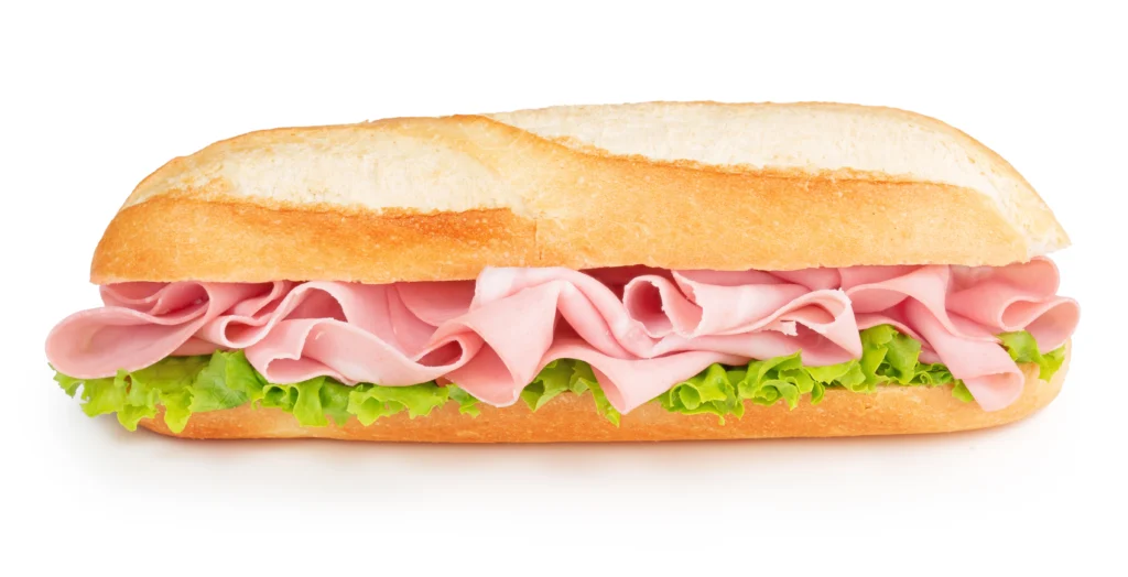 A fresh bologna sandwich with multiple layers of pink bologna and crisp green lettuce on a crusty baguette
