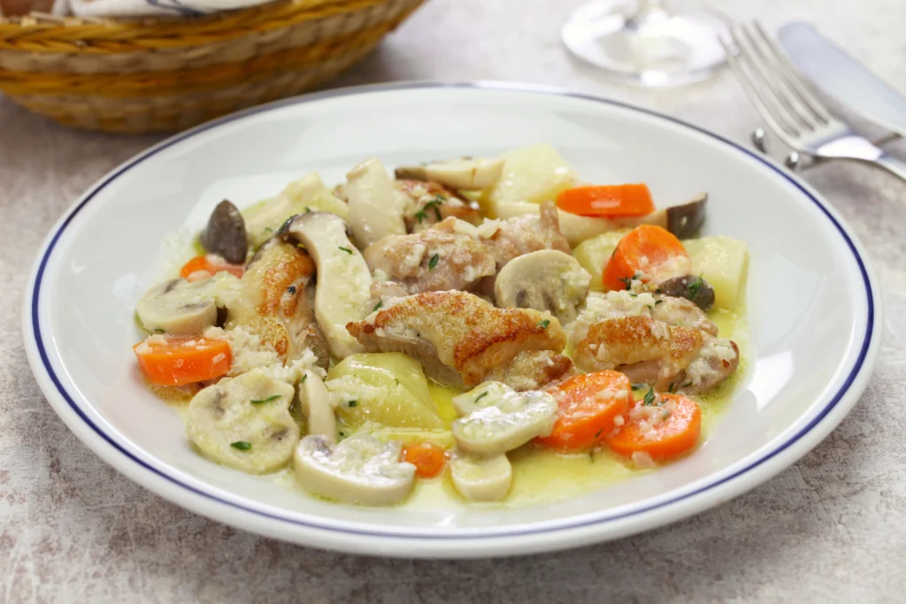 Close-up view of a creamy chicken and mushroom fricassee dish, featuring tender chicken pieces and sliced mushrooms in a rich, velvety sauce, garnished with fresh herbs.